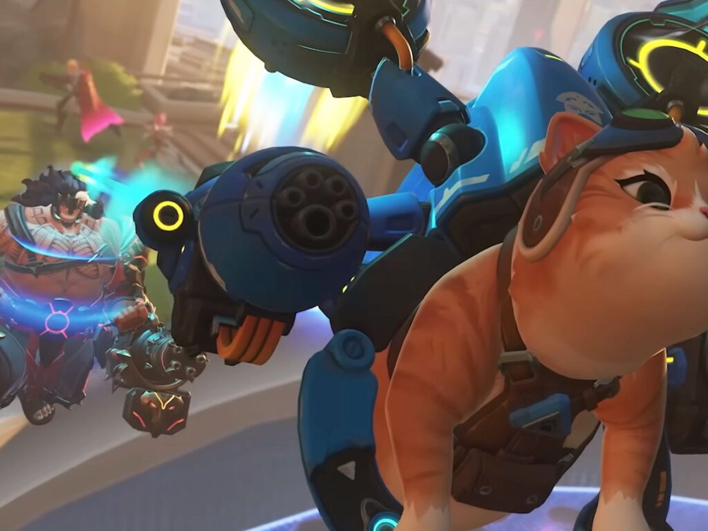 Overwatch 2 screenshot showing the Jetpack Cat hero with goggles and blue jetpack rig in the foreground while Bastion's blue sentry body and multi-barrel turret gun are mounted alongside, with a Mauga-like hero visible behind them on the map.