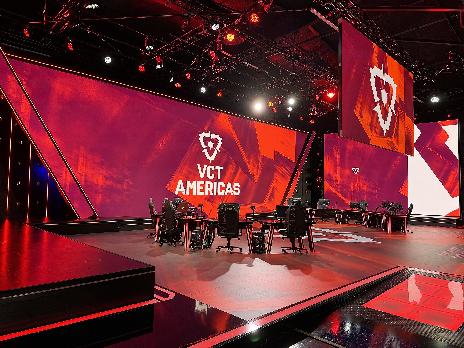 Valorant Champions Tour Americas stage at the Riot Games Arena, with red-lit screens displaying the VCT logo and empty player desks